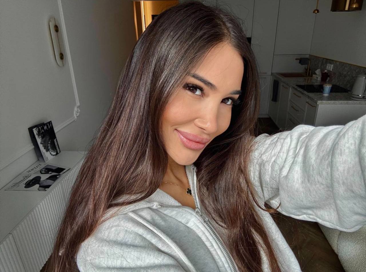 Kathy smiling in a cozy gray hoodie in a bright, modern apartment