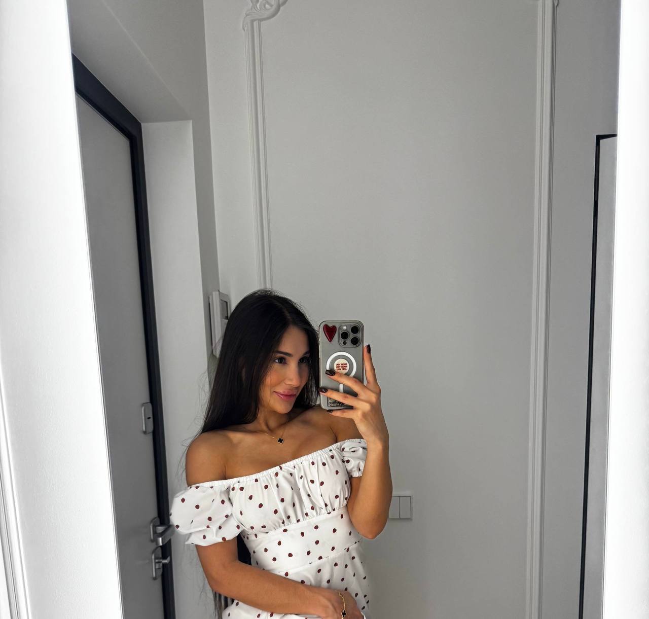 Kathy taking a mirror selfie in a white off-the-shoulder polka-dot dress